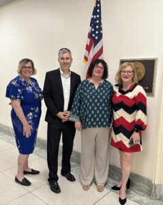 Three women and a man stand in front of the American flag